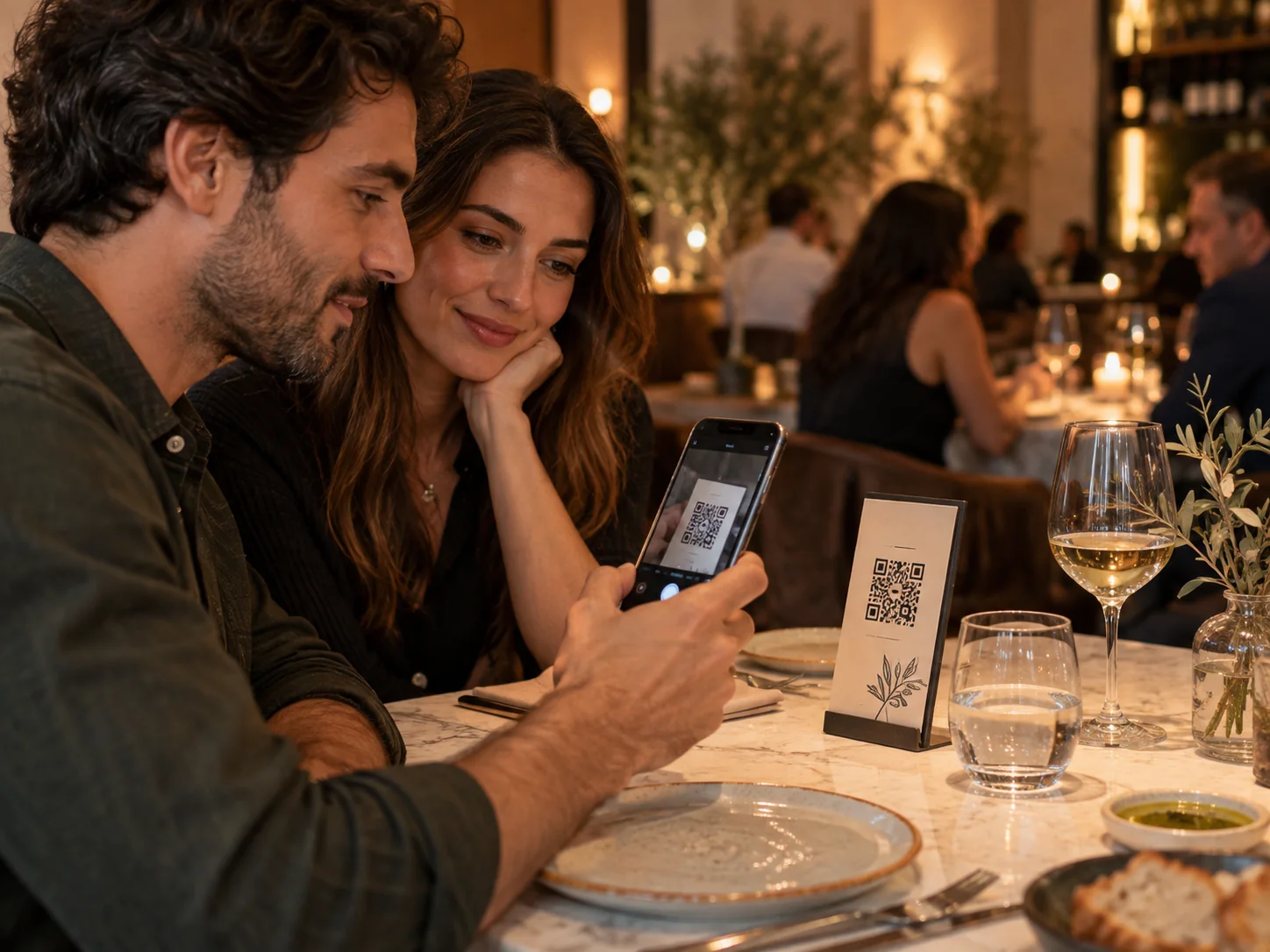 Una coppia al tavolo inquadra con il telefono il codice QR sul cartoncino per aprire il menù